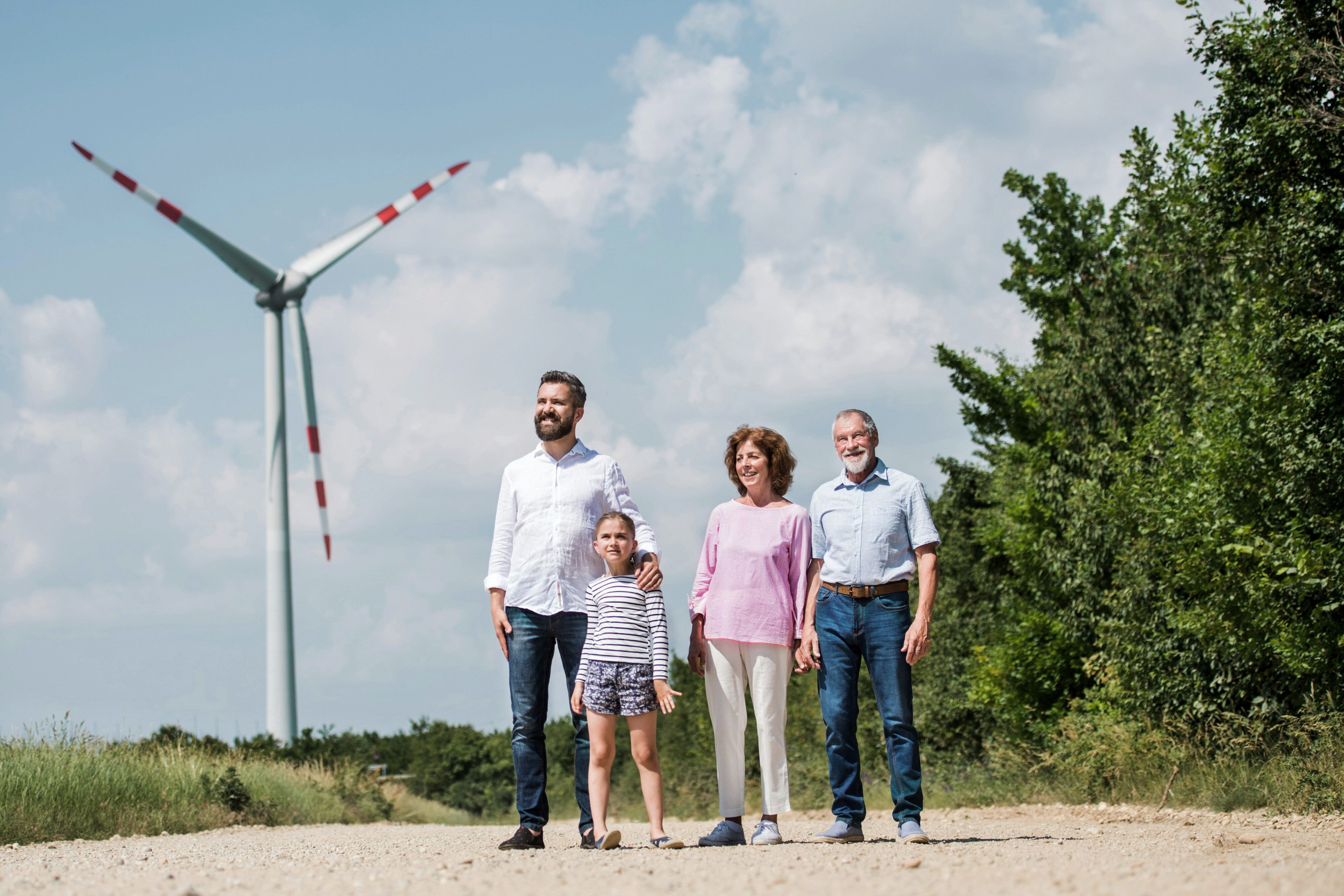Eine Familie steht am Waldrand. Im Hintergrund ist ein Windrad.